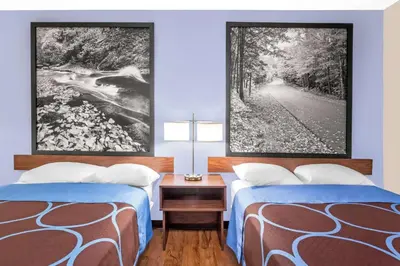 two beds in a room with two pictures on the wall at Super 8 by Wyndham Oneonta/Cooperstown in Oneonta