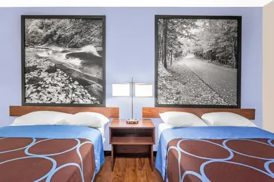 two beds in a room with two paintings on the wall at Super 8 by Wyndham Oneonta/Cooperstown in Oneonta