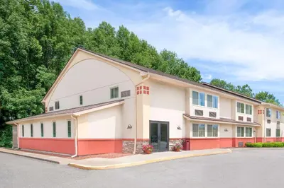 a large white and red building with trees in the background at Super 8 by Wyndham Oneonta/Cooperstown in Oneonta