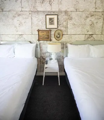 two beds with white sheets and a table with a lamp at The Little Lion in Great Barrington