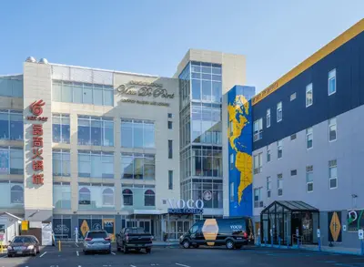 a large building with cars parked in a parking lot at voco Fiorello - LaGuardia Airport by IHG in Queens