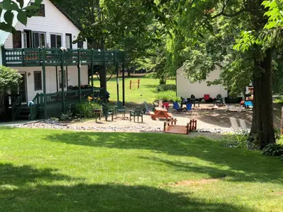 a yard with chairs and tables in front of a house at The Elms Waterfront Cottages in Lake Luzerne