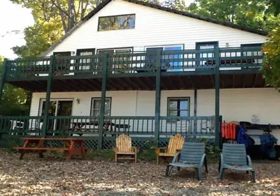a house with a deck with chairs and a table at The Elms Waterfront Cottages in Lake Luzerne