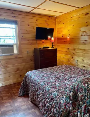 a bedroom with a bed and a flat screen tv at The Elms Waterfront Cottages in Lake Luzerne