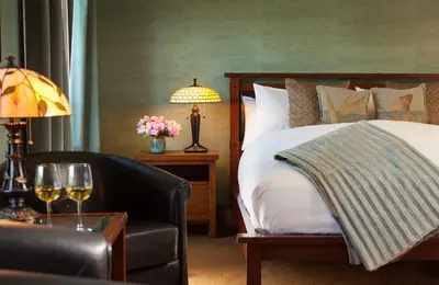 a hotel room with a bed and a chair and wine glasses at Settlers Inn in Hawley