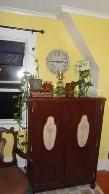 a wooden cabinet with a clock on a yellow wall at The Red Rooster in White Plains