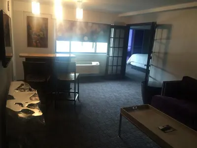a living room with a table and a room with a bed at The Royal Regency Hotel in Yonkers