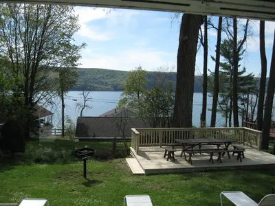 a picnic table and bench on a deck with a view of a lake at Hickory Grove Motor Inn - Cooperstown in Cooperstown