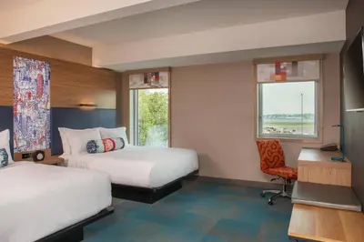 a hotel room with two beds and a desk and a chair at Aloft New York LaGuardia Airport in Queens