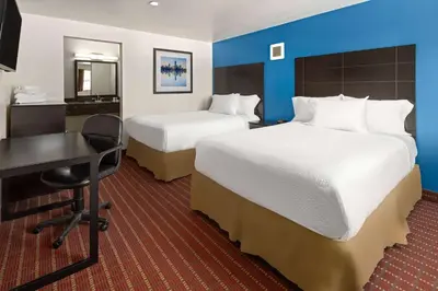 a hotel room with two beds and a desk at Travelodge by Wyndham Manhasset in Manhasset