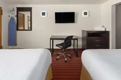 a bedroom with two beds and a desk with a chair at Travelodge by Wyndham Manhasset in Manhasset