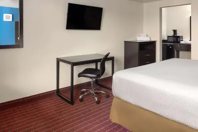 a hotel room with a desk and a bed and a bed and a chair at Travelodge by Wyndham Manhasset in Manhasset