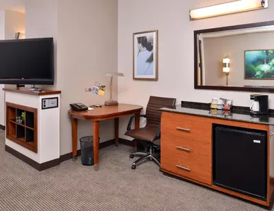a hotel room with a desk and a tv and a table at Hyatt Place Garden City in Garden City