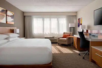 a hotel room with a large white bed and a desk at Delta Hotels by Marriott Utica in Utica