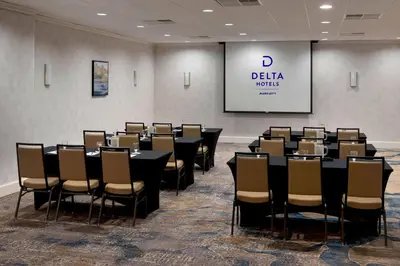a conference room with tables and chairs and a screen at Delta Hotels by Marriott Utica in Utica