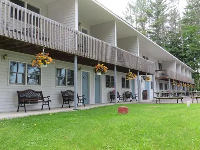 a large white house with benches on a lawn at Bayside Inn & Marina in Cooperstown