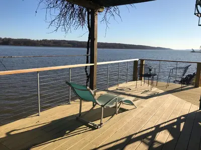 a green chair sitting on a deck next to the water at Hudson Riverfront Home in Catskill
