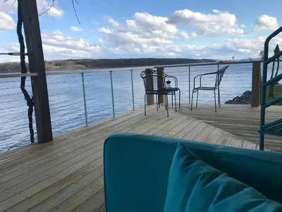 a deck with a table and chairs on the water at Hudson Riverfront Home in Catskill
