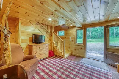 a living room with a tv and a staircase in a log cabin at Log Cabin Escape in Jacksonville