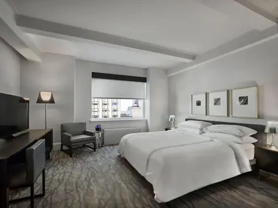 a white bedroom with a large white bed and a desk at AKA Central Park in New York