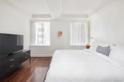 a white bedroom with a large bed and a flat screen tv at AKA Sutton Place in New York