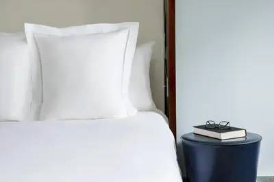 a bed with white pillows and a book on a stool at Royalton New York in New York