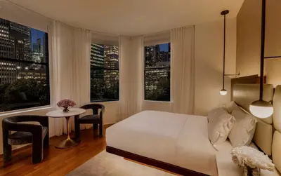 a bedroom with a bed and a table and windows at Bryant Park Hotel in New York