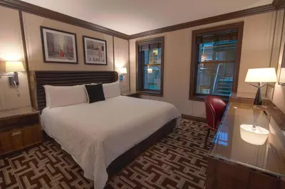 a bedroom with a bed and a desk and windows at Iroquois New York Times Square in New York