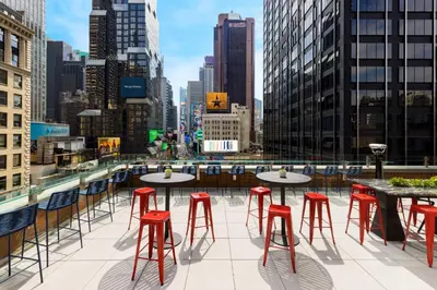 a rooftop patio with tables and red stools at M Social Hotel New York Times Square in New York