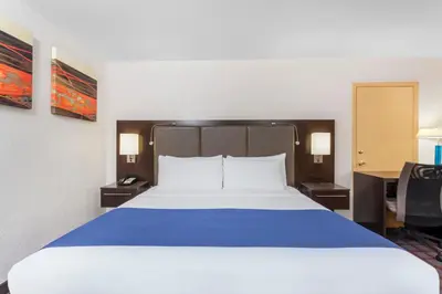 a large bed in a hotel room with a blue blanket at Days Inn by Wyndham Woodbury Long Island in Woodbury