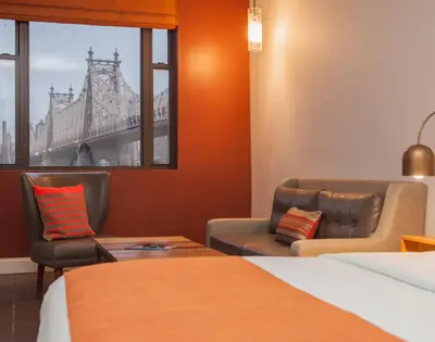 a room with two chairs and a bed and a window at Ravel Hotel Trademark Collection by Wyndham in Queens