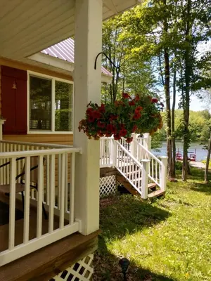 a porch with a white railing and a flower basket with red roses at Hidden Lakefront Retreat in Sherburne