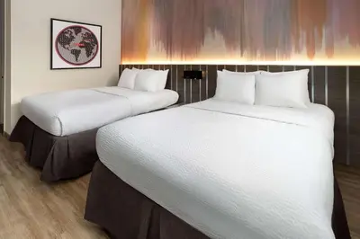 two beds in a hotel room with white sheets at Ramada by Wyndham Bronx in Bronx