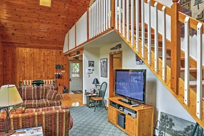 a living room with a tv and a staircase at Stamford Lakefront Home with Dock and Wraparound Deck! in Stamford