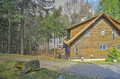 a log cabin with a man standing on the porch at Stamford Lakefront Home with Dock and Wraparound Deck! in Stamford