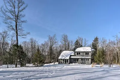 a house with snow covered roof in a snowy field at Berkshires Home on 11 Acres with Pond and 2 Fire Pits! in Becket