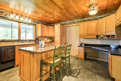a kitchen with wooden cabinets and a island with chairs at Thompson Home with Deck and Pond, 8 Mi to Elk Mountain in Thompson