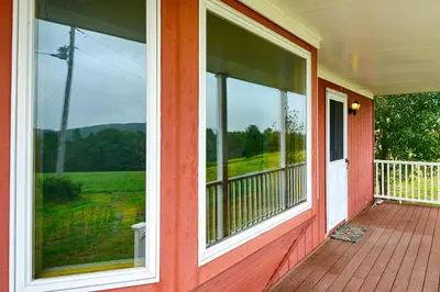 a red house with a porch with large windows at Mountain Top Country Hideaway 48 Acres, Fire Pit! in Leonardsville