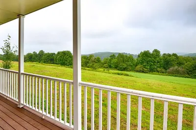 a porch with a view of a field and trees at Mountain Top Country Hideaway 48 Acres, Fire Pit! in Leonardsville