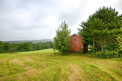 a red barn in the middle of a field at Mountain Top Country Hideaway 48 Acres, Fire Pit! in Leonardsville