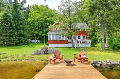 a wooden dock with two chairs and a house at Authentic 1912 Adirondack Lake Camp with Fire Pit in Stratford
