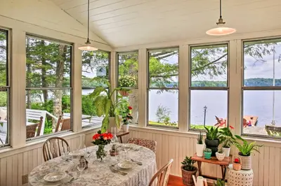a dining room with a table and windows at Authentic 1912 Adirondack Lake Camp with Fire Pit in Stratford