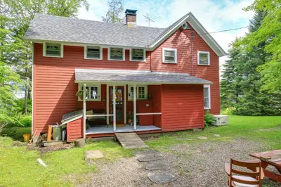a red house with a porch and a yard at Authentic 1912 Adirondack Lake Camp with Fire Pit in Stratford