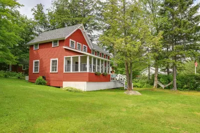 a red house in a field with a yard at Authentic 1912 Adirondack Lake Camp with Fire Pit in Stratford