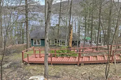 a house in the woods with a wooden deck at Dainty New Preston Cottage with Dock and Lake Views! in New Preston