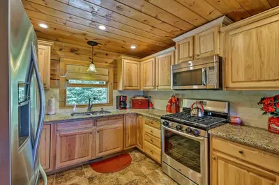 a kitchen with wooden cabinets and a stove top oven at Jacksonville Cabin with Wraparound Deck and Views in Jacksonville
