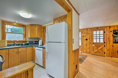 a kitchen with a white refrigerator and wooden cabinets at Picturesque Cottage with Sunroom on Ashmere Lake! in Hinsdale