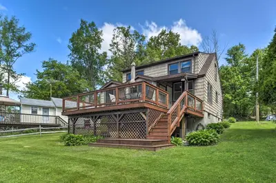 a large house with a deck on a lawn at Picturesque Cottage with Sunroom on Ashmere Lake! in Hinsdale