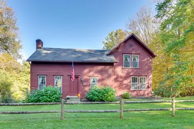 a red house with a fence in front of it at Tranquil 3 BR Stockbridge House with Private Deck! in Stockbridge