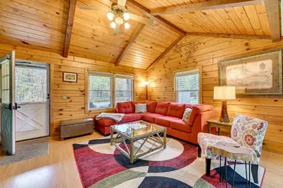 a living room with a red couch and a table at High Peak Heaven Cozy Log Cabin on 1 Acre! in Windham
